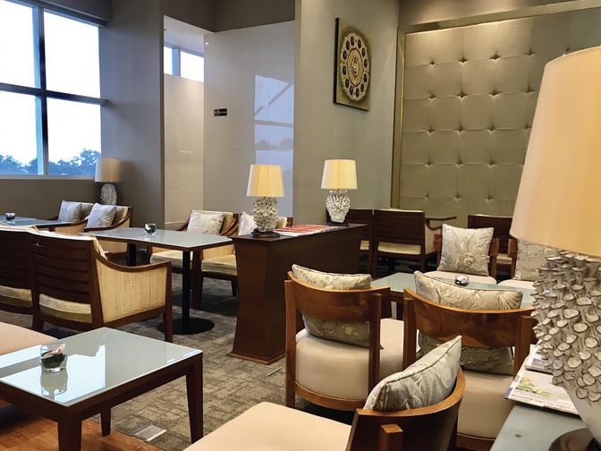 Seating area in The Coral Executive Lounge at Chiang Mai International Airport features cushioned chairs, glass tables, and decorative lamps.