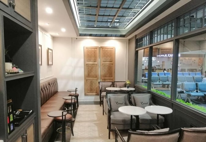 The Coral Executive Lounge at Mae Fah Luang International Airport features booth and table seating with views of the terminal area.