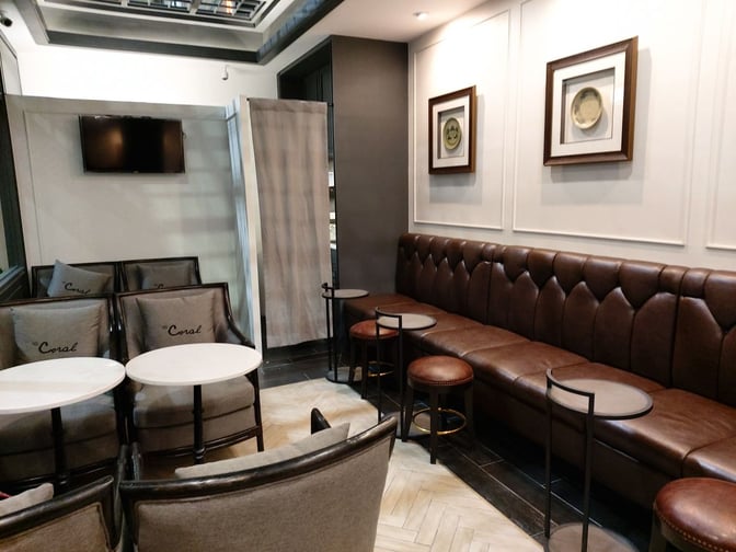 The seating area in The Coral Executive Lounge at Mae Fah Luang International Airport features cushioned chairs, a long bench, and small tables.