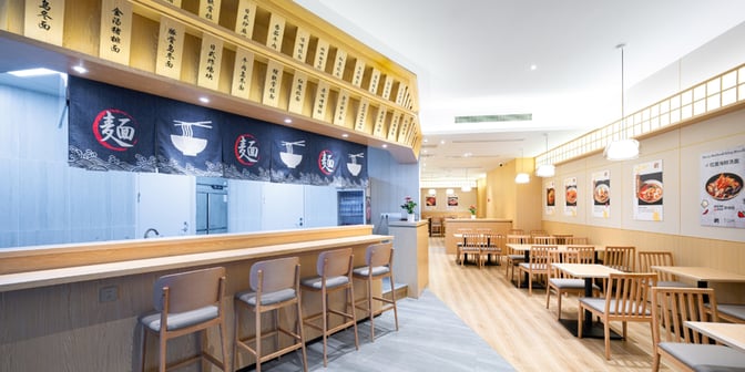 The dining area in the Plaza Premium Lounge at Chongqing Jiangbei International Airport features counter seating and tables with noodle-themed decor.
