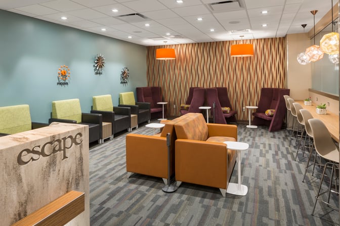 The seating area in the Escape Lounge at Cincinnati/Northern Kentucky International Airport features armchairs, sofas, and counter seating with small tables.