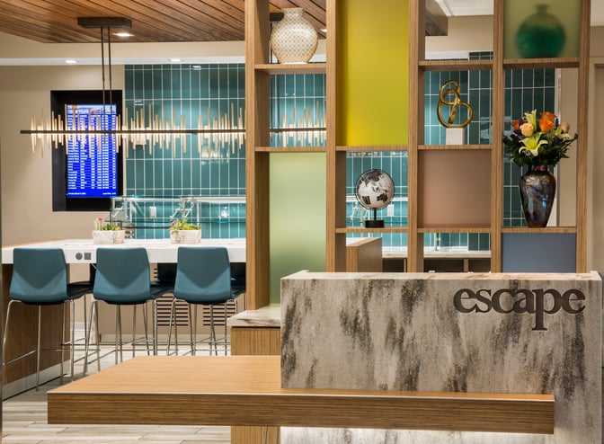 The Escape Lounge at Cincinnati/Northern Kentucky International Airport features a reception area with decorative shelving and seating near a flight information display.