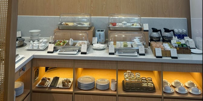 The SH Premium Lounge at Con Dao Airport offers a self-serve food station with covered dishes, beverages, and tableware for guests.