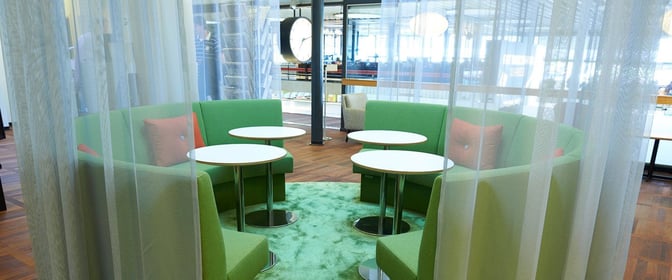 Semi-private seating area in the Aspire Lounge at Copenhagen Airport features circular booths and tables, offering a comfortable space for travelers.