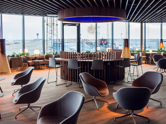 The Eventyr Lounge at Copenhagen Airport features a seating area with swivel chairs and tables, offering views of the airport runway.