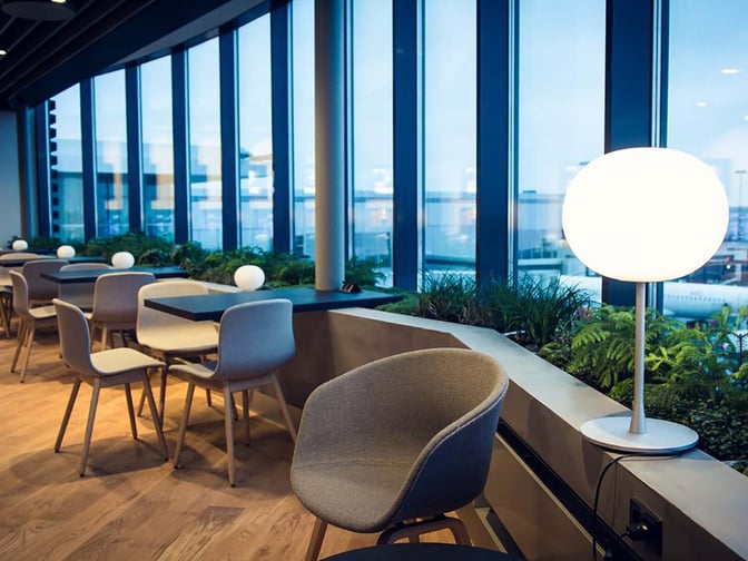 Seating area in Eventyr Lounge at Copenhagen Airport features tables and chairs with views of the tarmac through large windows.