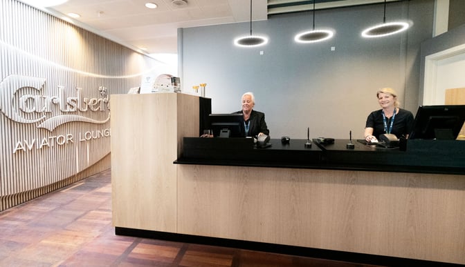 The reception area of Carlsberg Aviator Lounge at Copenhagen Airport features a check-in desk with staff ready to assist travelers.