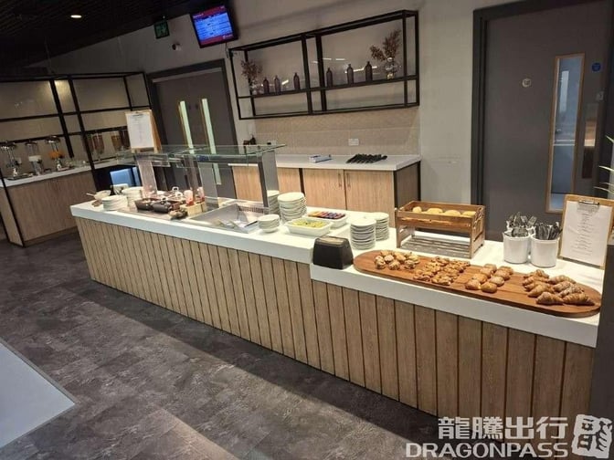 Self-serve breakfast station at The Kinsale Lounge, Cork Airport, offers pastries, cereals, and beverages with plates and utensils available.