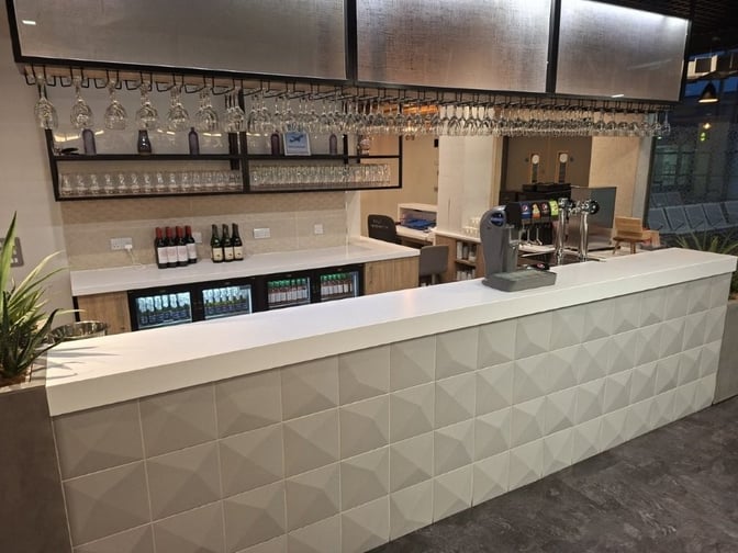 The bar at The Kinsale Lounge in Cork Airport offers a selection of wines, spirits, and beers with glassware displayed overhead.
