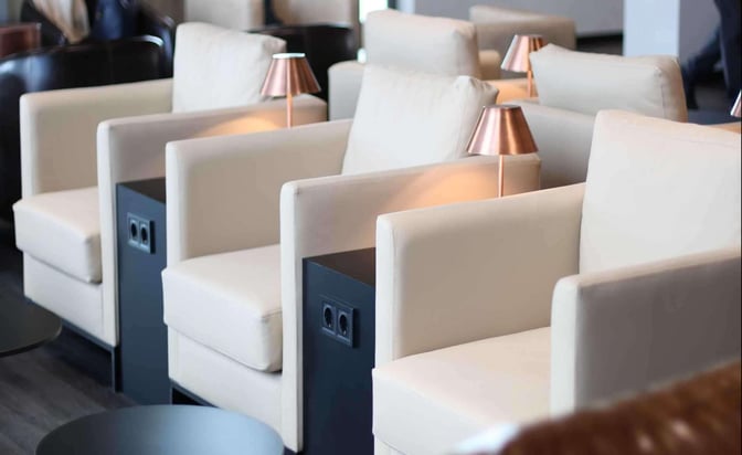 Comfortable seating at Celebi COV Domestic Lounge features individual armchairs with side tables, lamps, and accessible power outlets for travelers.