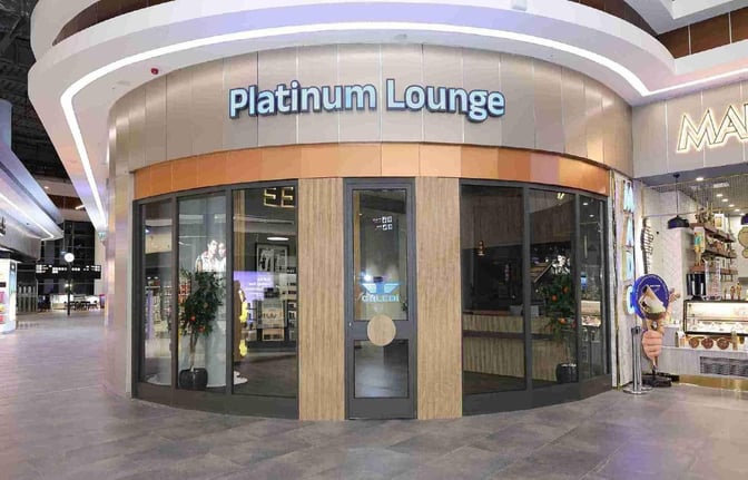The entrance to the Platinum Lounge at Cukurova International Airport features glass doors and is located near retail shops.