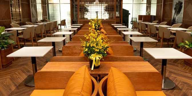 The seating area in SH Premium Lounge Da Nang features individual tables and chairs with decorative floral arrangements for travelers.