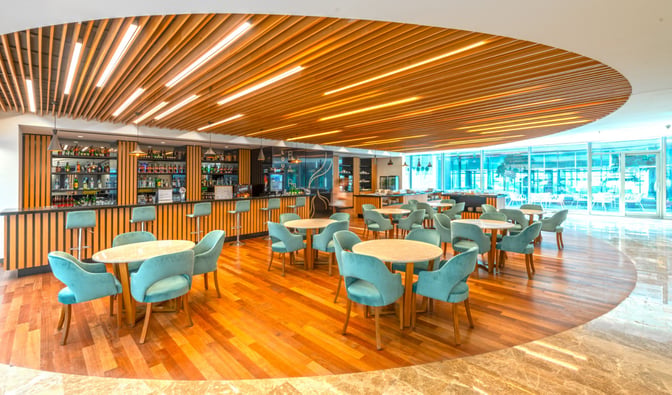 The CIP Lounge at Dalaman Airport features a bar with a variety of beverages and a seating area with round tables.