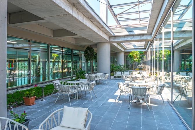 The CIP Lounge at Dalaman Airport features an outdoor seating area with tables and chairs surrounded by greenery and glass walls.