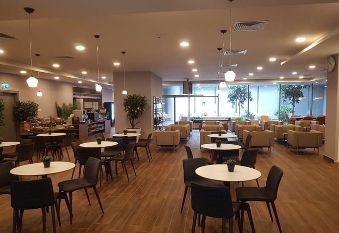 The DLM Lounge at Dalaman Airport features a seating area with round tables, chairs, and a self-serve food station.