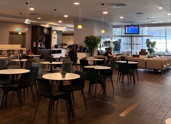 The DLM Lounge at Dalaman Airport features a spacious seating area with round tables and chairs, offering views of the tarmac.