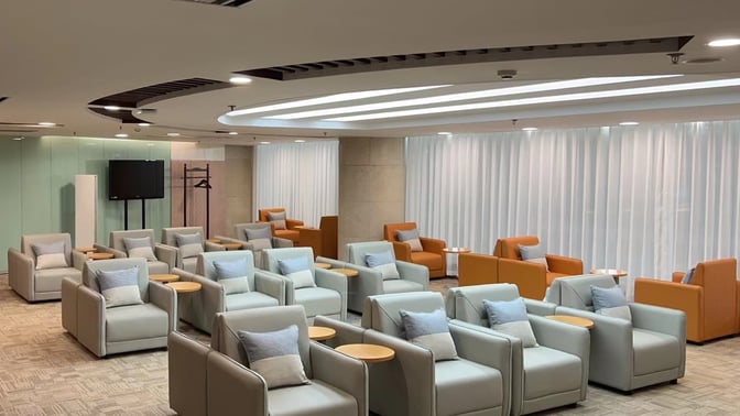 The seating area in the Business Travel Lounge at Dalian Zhoushuizi International Airport features arranged armchairs with side tables and a television.