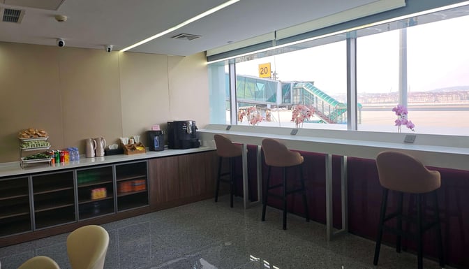 The VIP Lounge at Dalian Zhoushuizi International Airport features a self-serve snack and beverage area with counter seating overlooking the tarmac.