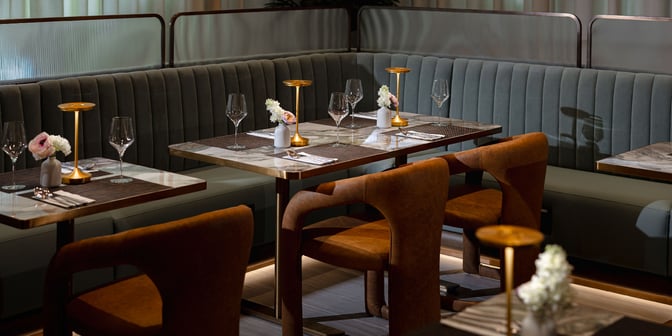 Booth seating in the Plaza Premium First Lounge at Dallas-Fort Worth International Airport features tables set with glassware and small floral arrangements.