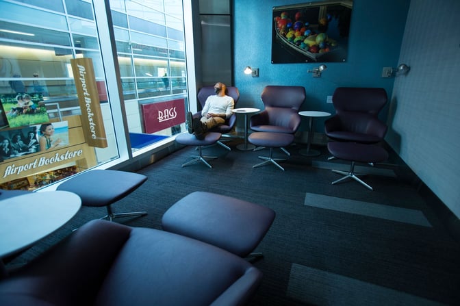 Seating area in The Club DFW lounge features comfortable chairs with footrests and side tables, overlooking the airport.