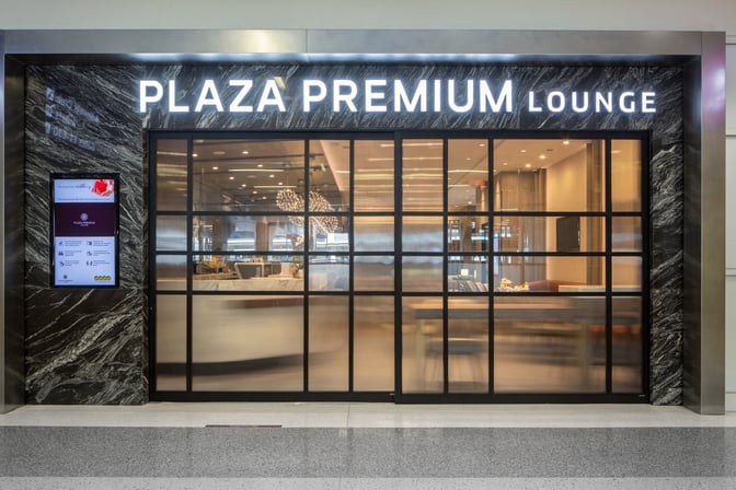 The entrance to the Plaza Premium Lounge at Dallas-Fort Worth International Airport features a glass facade and digital information display.