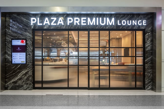 The entrance to the Plaza Premium Lounge at Dallas-Fort Worth International Airport features a glass facade and digital information display.