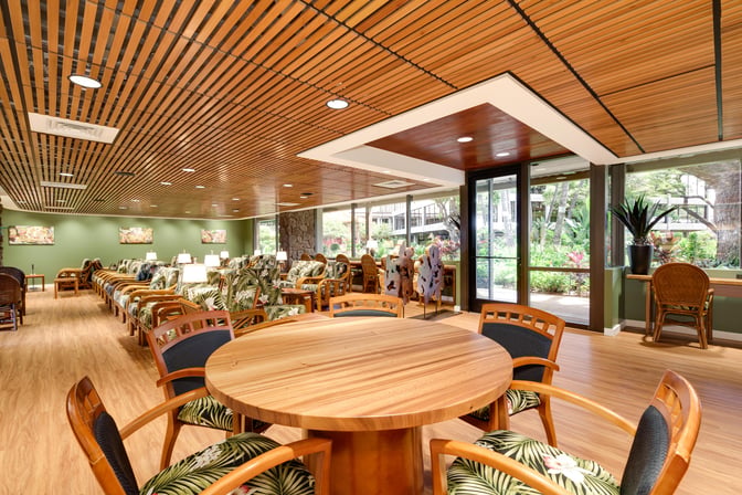 The IASS Hawaii Lounge at Daniel K. Inouye Honolulu International Airport features a seating area with tables and chairs overlooking a garden view.