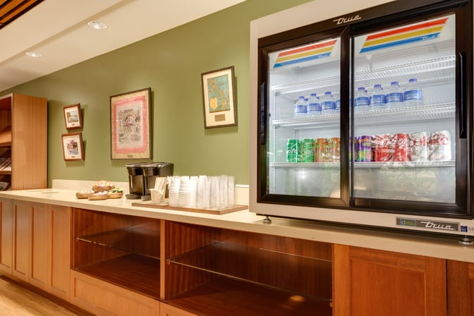 The IASS Hawaii Lounge at Daniel K. Inouye Honolulu International Airport features a refreshment area with a beverage fridge and coffee station.