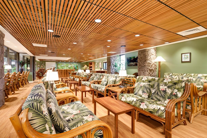 The IASS Hawaii Lounge at Daniel K. Inouye Honolulu International Airport features seating with floral-patterned cushions and wooden tables for relaxation.