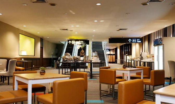 Seating area in Miracle Lounge No. 1 at Don Mueang Airport features tables and chairs with nearby self-serve food stations.