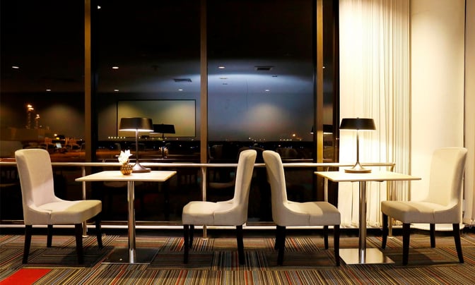 Seating area in Miracle Lounge No. 1 at Don Mueang International Airport features tables with chairs and lamps, offering runway views.