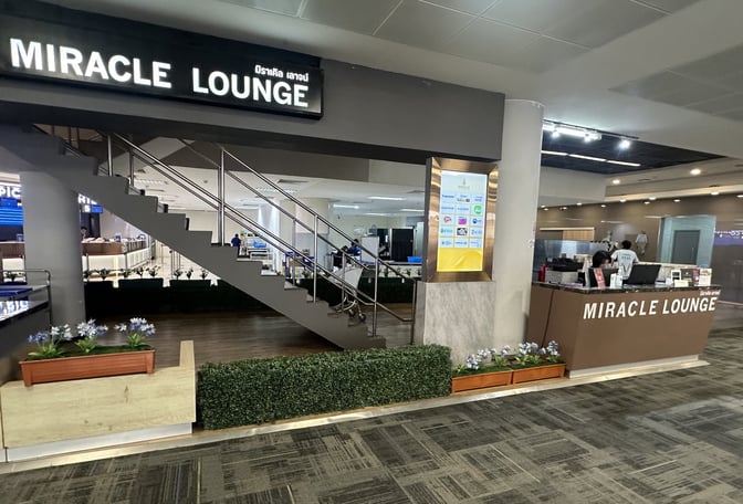 The entrance to Miracle Lounge at Don Mueang International Airport features a reception desk and a staircase leading to the lounge area.