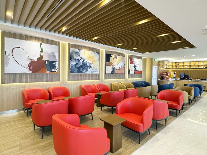 The Travel Club lounge at Don Mueang International Airport features comfortable seating with individual tables and a self-serve beverage station.