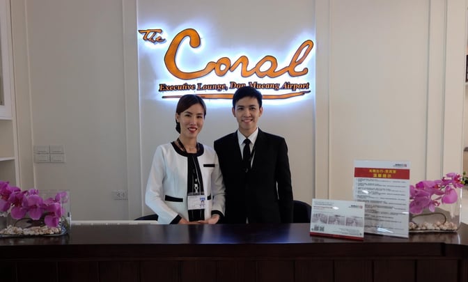 The reception desk at The Coral Executive Lounge, Don Mueang Airport, features staff ready to assist guests with check-in.