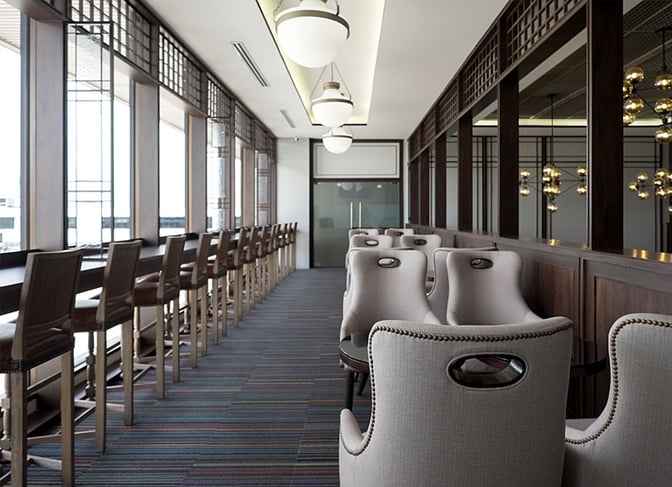 Bar seating at The Coral Forest Lounge, Don Mueang Airport, features high stools along a window counter and cushioned chairs for relaxation.