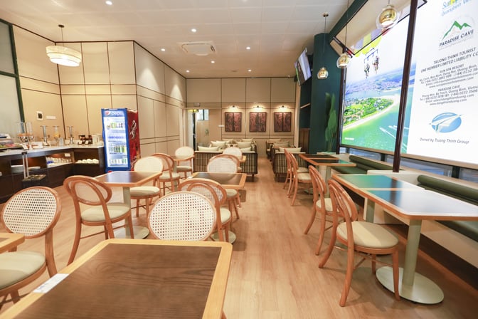 The SH Premium Lounge at Dong Hoi Airport features a seating area with tables and chairs, and a self-serve beverage station.
