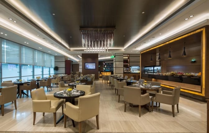 The Ahlan First Class Lounge at Dubai International Airport features a dining area with table seating and a self-serve food station.