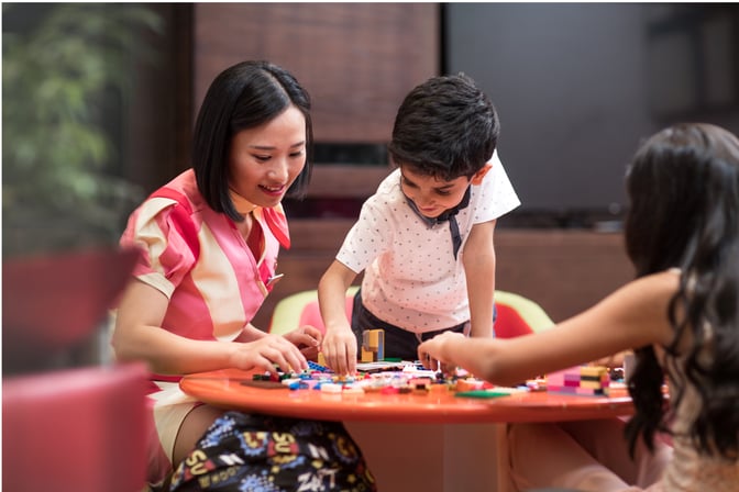 Children and an adult engage in a play area at marhaba Lounge, Dubai International Airport Concourse D, using colorful building blocks on a table.
