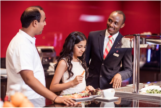 A staff member at marhaba Lounge, Dubai International Airport Concourse D, assists guests at a self-serve food station with various dishes.