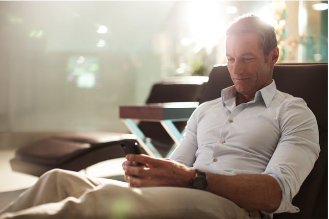 A person is seated in a lounge chair at the marhaba Lounge, Dubai International Airport, Terminal 2, using a smartphone.