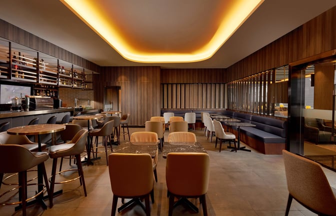 The Plaza Premium Lounge at Dubai International Airport features a bar with high stools and a seating area with tables and chairs.
