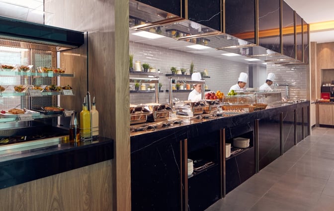 The food area at Plaza Premium Lounge, Dubai International Airport, features a buffet with chefs preparing fresh dishes and self-serve options.