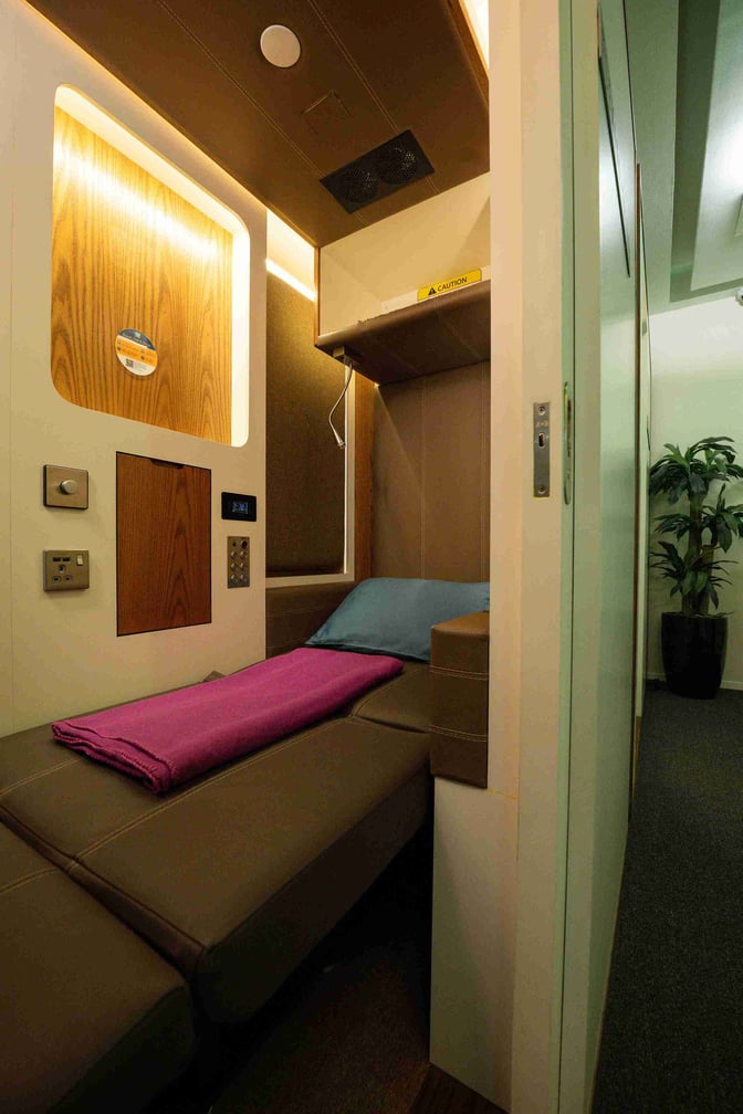 A sleep pod at Dubai International Airport's Concourse C offers a private resting space with a bed, pillow, and blanket.