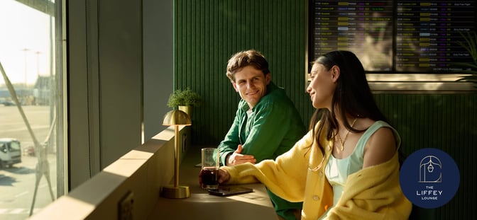 Seating at The Liffey Lounge in Dublin Airport offers views of the runway, with a flight information screen nearby.