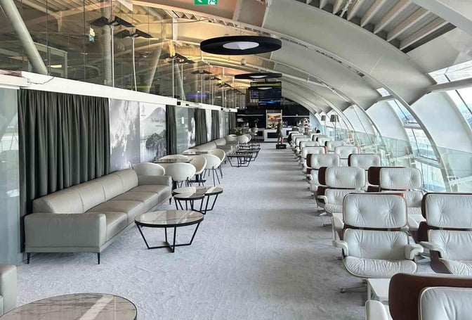 The Sky Lounge at Dubrovnik Airport features a spacious seating area with sofas, armchairs, and round tables along a glass wall.