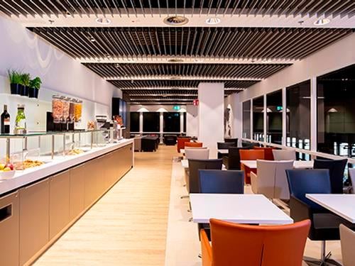 The Open Sky Lounge at Dusseldorf Airport features a self-serve food area with various seating options and large windows.
