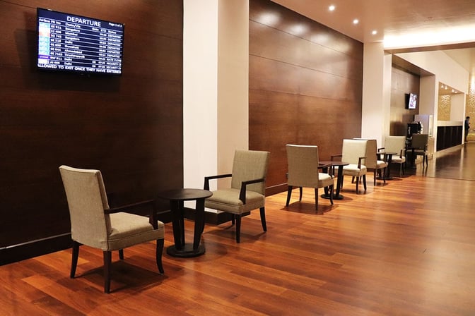 The seating area in Earth Lounge at Cochin International Airport features chairs and tables with a departure information screen.