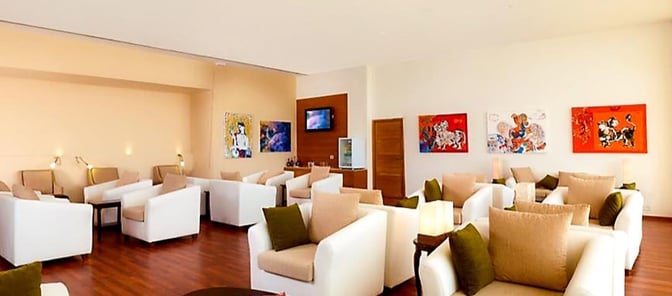The Earth Lounge at Cochin International Airport features comfortable seating with armchairs and tables, complemented by wall art and a television.