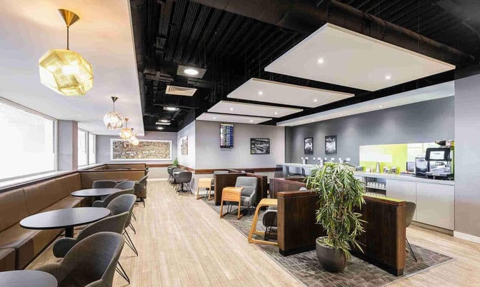 The seating area in the Escape Lounge at East Midlands Airport features round tables, chairs, and semi-private booths with a refreshment station.