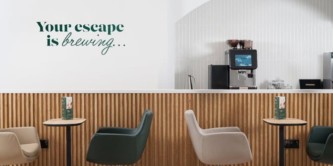 The coffee station at East Midlands Airport's Escape Lounge features a self-serve machine with seating and informational menus on tables.